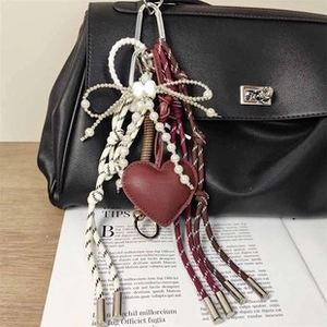 Dettaglio di ciondolo cuore in pelle rossa con fiocco di perle su borsa nera