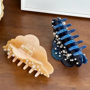 Heavy-duty pearl acetate hair claw clips in amber and dark blue on dark wood surface