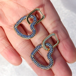 Dettaglio di orecchini a cuore in oro 18K con zirconi blu tenuti in una mano
