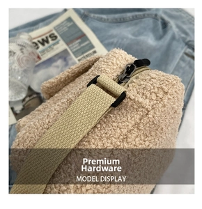 Close-up of beige faux shearling bag featuring metallic zipper and woven shoulder strap