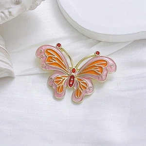 Detalle de broche de mariposa en esmalte rosa y naranja con bordes dorados en seda