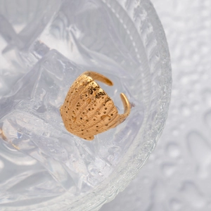 Macro detail of 18K gold plated conch shell ring on a cool ice-like textured surface