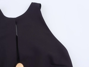 Detail van zwarte mini-jurk met een decoratieve ronde goudkleurige metalen knoopsluiting