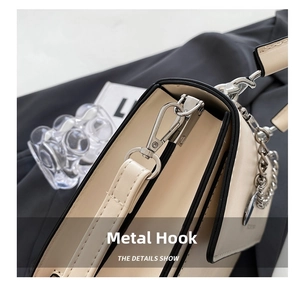 Close-up of sleek silver metal hook hardware and black edge paint on a beige crossbody bag
