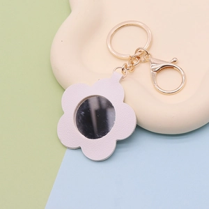 Detail shot of white leather flower keychain with integrated mirror and gold metal clasp