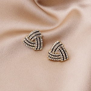 Detailed macro of gold triangular stud earrings with white crystals and black enamel lines