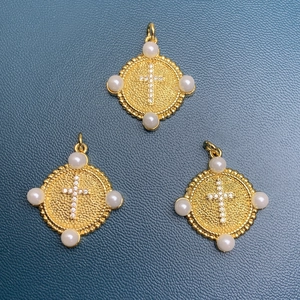 Golden round cross pendants with small crystals and four surrounding pearls on blue surface