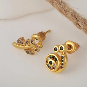 Macro shot of asymmetric gold earrings with colorful zircon leaves and spiral details