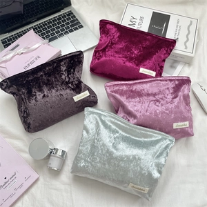 Flat lay of velvet makeup bags in multiple colors with lifestyle accessories on white fabric