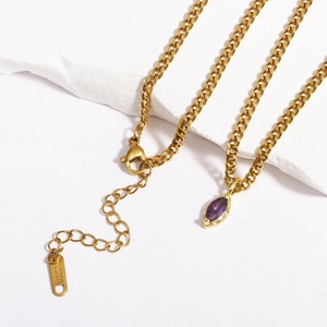 Macro detail of gold stainless steel necklace featuring a purple marquise cut gemstone