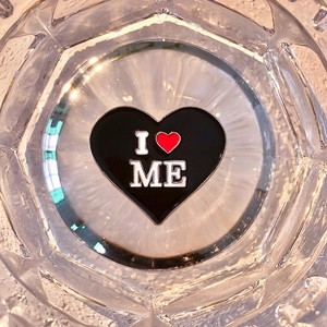 Macro shot of black enamel heart-shaped brooch featuring the I Love Me slogan engraving