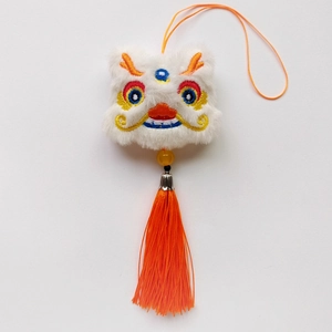 Gros plan du pendentif lion dansant en peluche blanche avec broderie et pompon orange