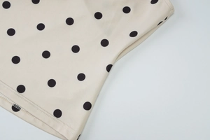 Detailaufnahme des cremefarbenen Stoffes mit schwarzen Punkten und feiner Overlock-Naht