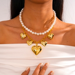 Detail of layered gold chain necklace with white pearls and five 3D heart-shaped charms
