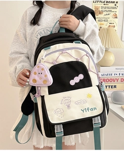 Detail of black and white school backpack featuring green straps and purple mushroom pouch
