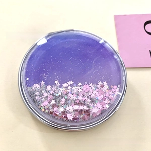 Close-up of folding pocket mirror featuring purple liquid quicksand and pink star sequins
