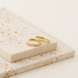 Close-up of gold hoop earrings with small zircon stones on a beige stone surface
