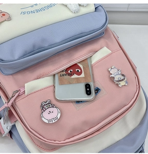 Detail of multi-color backpack showing front zipper pocket, decorative badges, and pendants