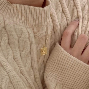 Detail of a vintage gold necklace with square rose pendant on a warm knit sweater