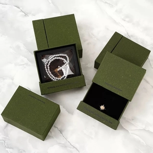 Detail of dark green matte jewelry boxes with gold foil text on white marble surface