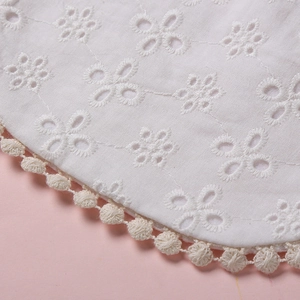 Détail du tissu en coton brodé blanc avec une bordure de dentelle à pompons beige