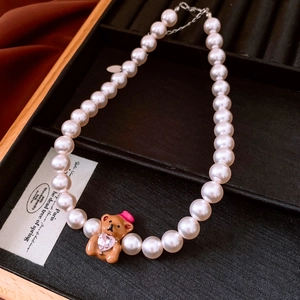 Detail of pearl necklace featuring a cute brown bear pendant holding a pink heart crystal