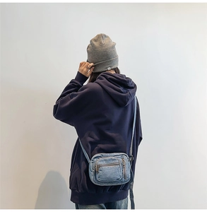 Detail view of light blue denim crossbody mini bag with multiple zipper pockets on a model