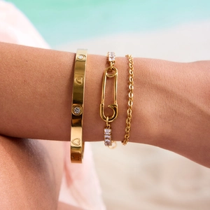 Close-up of gold-plated bracelets featuring crystal safety pin and screw pattern on wrist