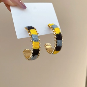 Detail of C-shaped hoop earrings featuring yellow and grey braided thread on golden metal