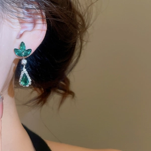 Close-up of elegant silver drop earrings with green teardrop crystals on model