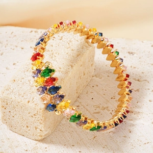 Elegant gold open bangle with colorful zircon stones on textured stone with beige background