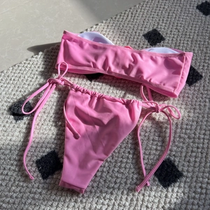Flat lay of pink strapless bikini set with drawstring side ties on a textured rug