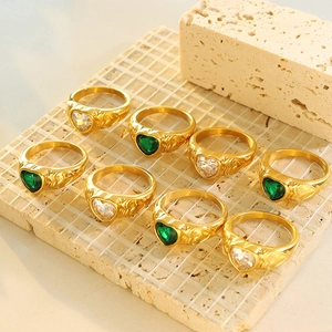 Gold-plated heart crystal rings with emerald and clear stones on stone background