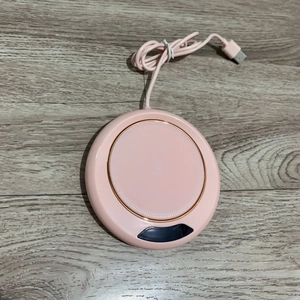Pink circular USB smart cup warmer on light wood surface with digital display