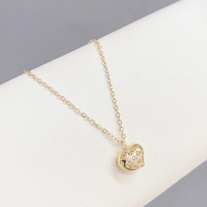 Close-up of golden heart pendant with hollow dots on a textured display background