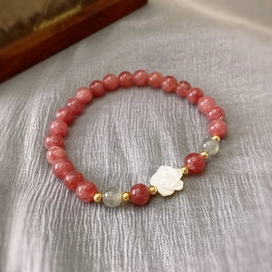 Detail view of pink strawberry crystal beads with white shell rose pendant on a beaded bracelet