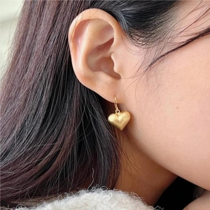 Elegant gold heart earrings with brushed matte finish on a female model
