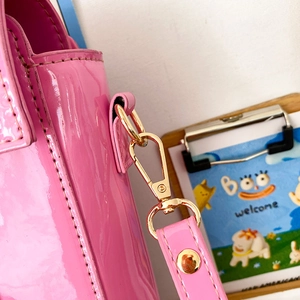 Detail of bright pink patent leather bag with gold D-ring and shoulder strap hook