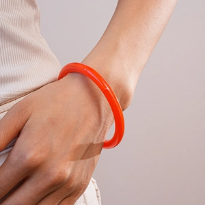 Détail d'un bracelet jonc en acrylique orange translucide au poignet du mannequin