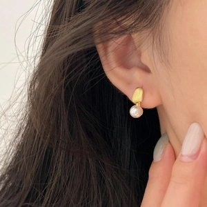 Close-up of matte gold irregular stud earring with a lustrous round white pearl on ear