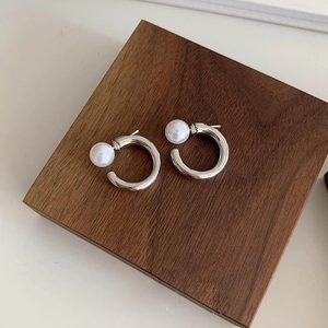 Elegant silver C-shaped pearl hoop earrings displayed on a dark wooden block