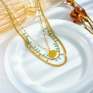 Three-layer gold titanium steel necklace with blue beads and round pendant on ceramic plate