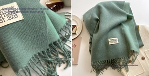 Detail of sage green cashmere-like scarf with long fringe and elegant woven brand label