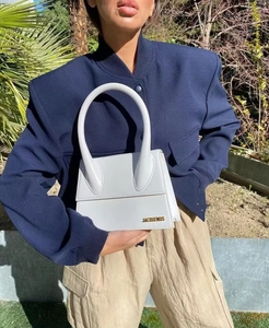 Close-up of white structured leather handbag with unique round handle and gold lettering