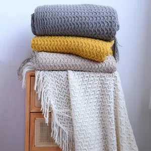 Knitted throw blankets in gray, yellow, and beige with wave patterns and tassel details
