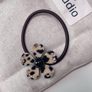 Macro shot of leopard print acetate flower hair tie with rhinestones on beige fabric