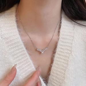 Close-up of V-shaped pearl pendant necklace with silver finish on model in white knit