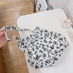Flat lay of a white floral canvas tote bag with black flower patterns and a wide strap