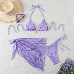 Three-piece purple floral bikini set with halter top and sarong on soft plush background
