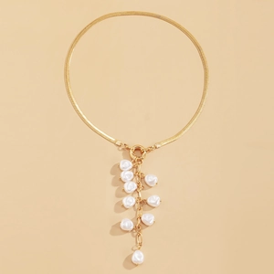 Detail of golden snake chain necklace with white baroque pearl tassels on beige background